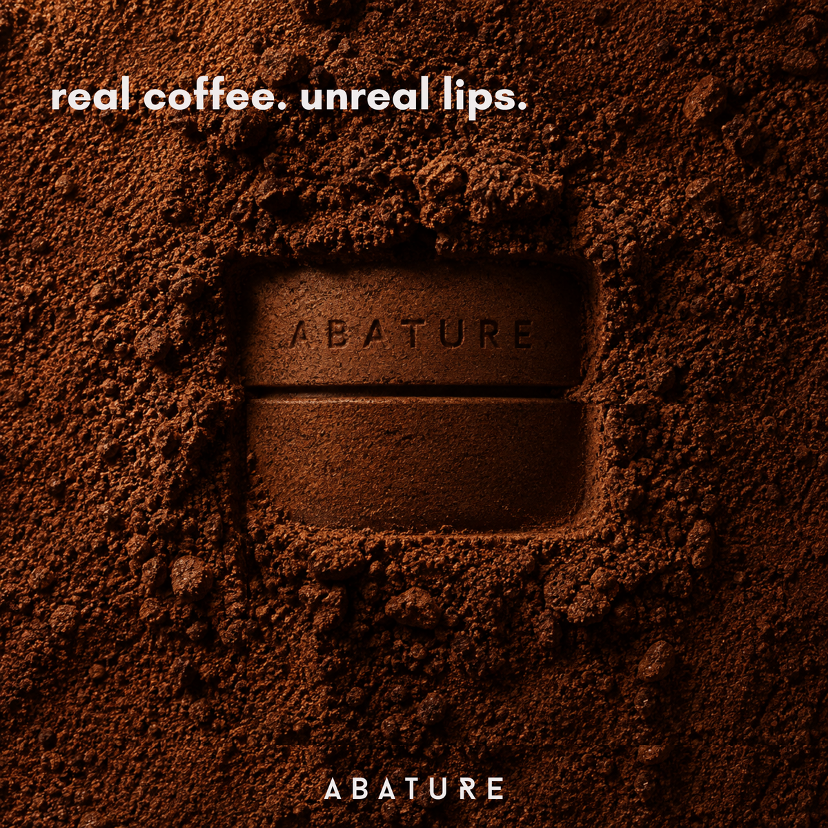 A close-up of a dark brown lip balm product embedded in or pressed into a bed of coffee powder, with the text 'real coffee. unreal lips.