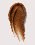 A textured swipe of coffee sugar scrub on a clean, light off-white background.