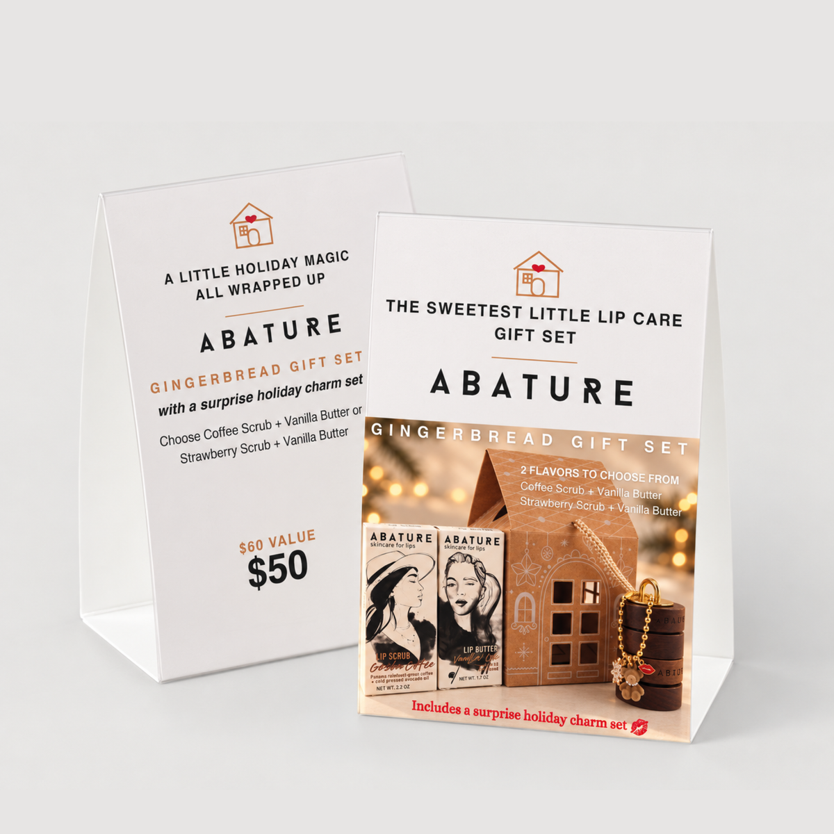 Two white A-frame display cards for Abature Gingerbread Gift Set on a light gray background. The front card shows the product branding, flavor description, and a small holiday-themed illustration with lip balm and a gingerbread houses.